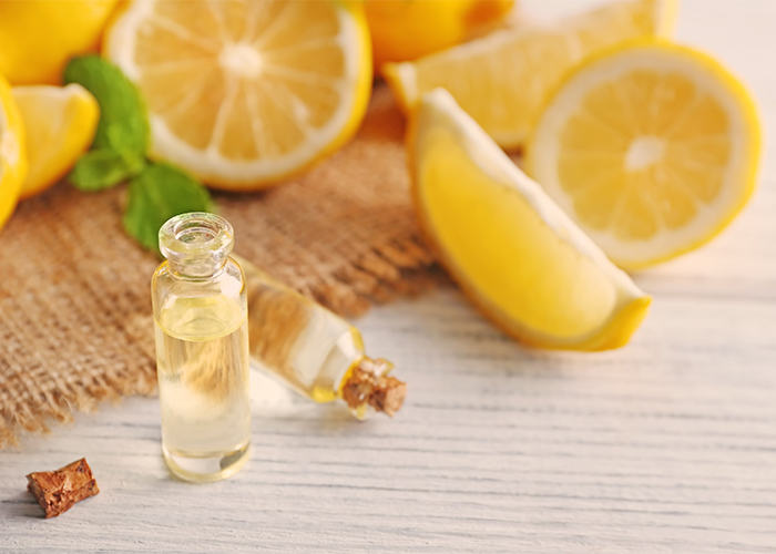 Small bottles of home-poured lemon essential oil with cork stoppers in front of a pile of cut lemons