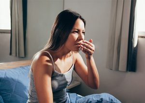 Woman sitting up on her bed putting her hand to her mouth to check her bad Keto breath