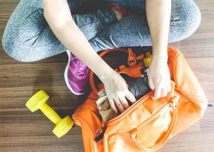 A woman packing her gym bag with gym clothes and dumbbells ready for a workout 