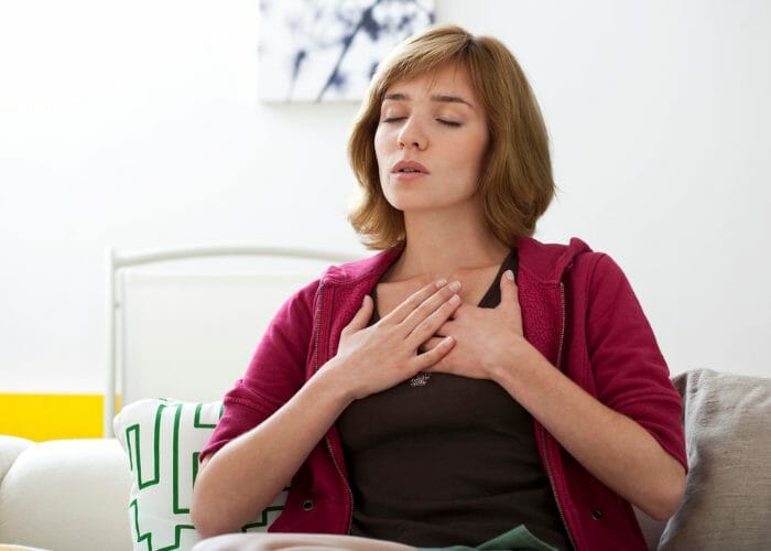 Woman with both hands on her chest practicing 4-7-8 breathing technique at home