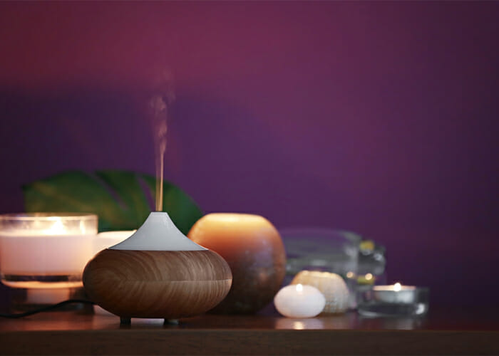 An aromatherapy oil diffuser surrounded by different types of candles on a bedside table