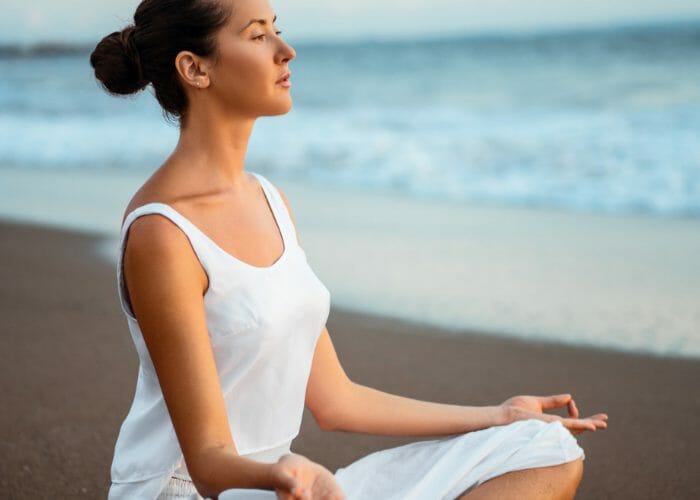 Woman sitting on the sand with the sea in the background in the middle of a meditation practice