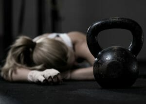 an exhausted woman resting on the floor with a kettlebell in the foreground