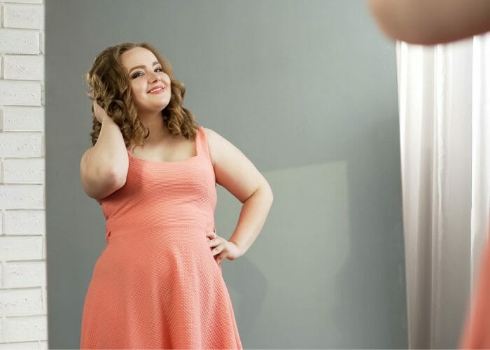 Body positive overweight woman striking a pose in the mirror and smiling with confidence
