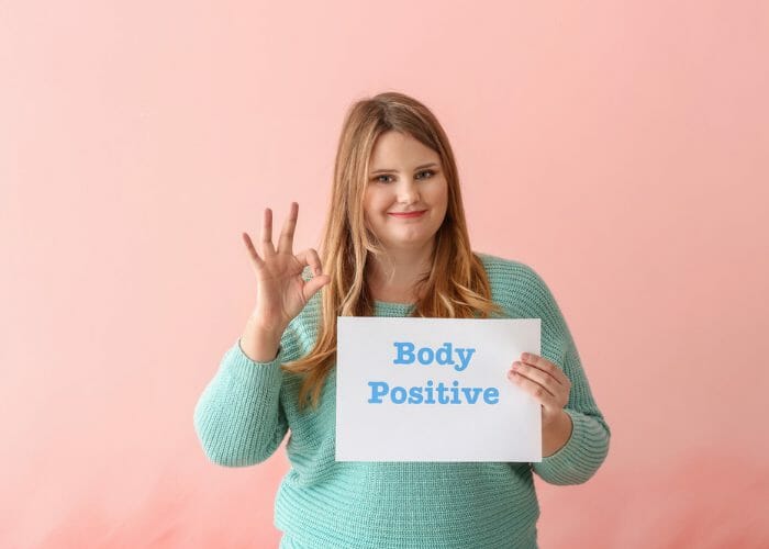 Plus size woman holding up a body positive sign and making the OK sign with her hand