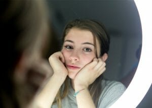 Teenage girl looking sad in a beauty mirror after being fat shamed