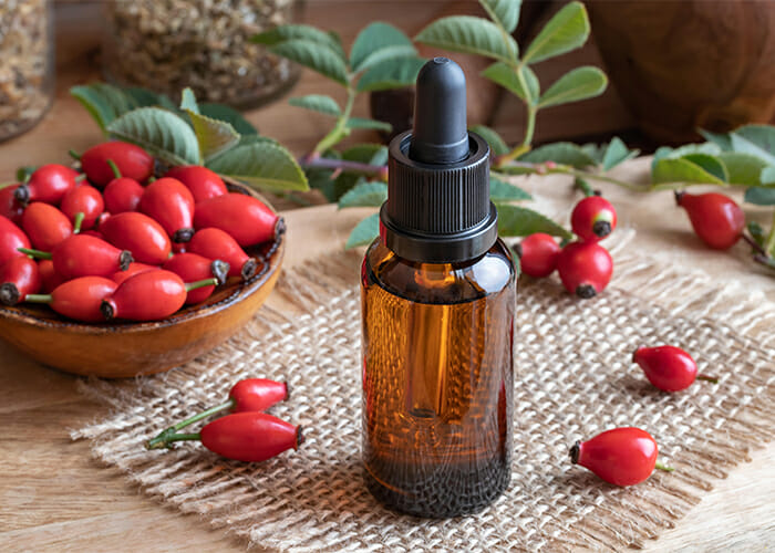 A dropper bottle of rosehip seed oil surrounded by rosehip fruits 