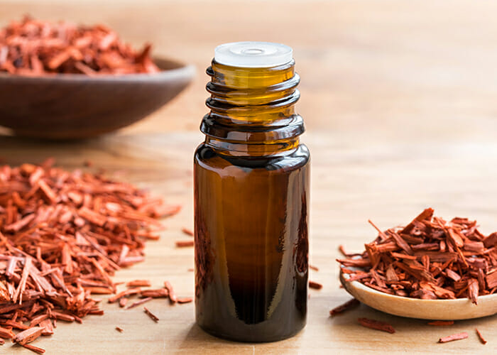 A close up of a sandalwood essential oil next to piles of sandalwood