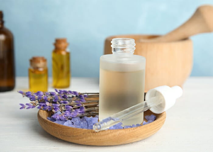 A cloudy bottle of lavender essential oil with a dropper on a wooden plate filled with lavender bath crystals and sprigs of lavender