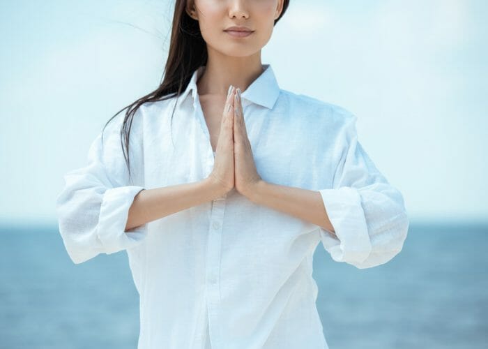 Woman in a white shirt standing by the seaside practicing breathing exercises
