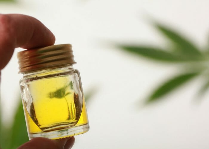 closeup of hand holding cbd cannabis oil in a small clear bottle