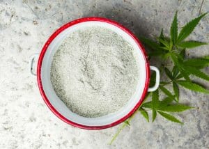 cbd cannabis powder in a red bowl with cannabis leaves beside it
