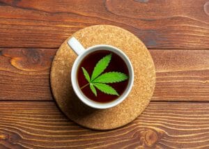 marijuana leaf floating in a cup of tea on wooden table