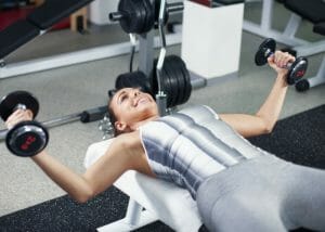 woman smiling and doing chest exercises with weights