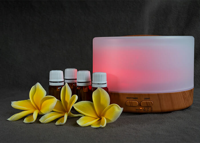 Amber colored bottles of a homemade bergamot essential oil diffuser recipe next to an electric diffuser and fresh flowers 