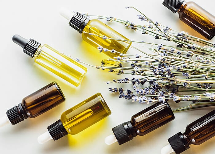 Clear and amber colored bottles filled with bergamot essential oil lavender essential oil, and lemon essential oil next to sprigs of dried lavender