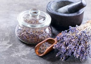 A glass jar filled with dry lavender next to sprigs of dried lavender and a pestle and mortar