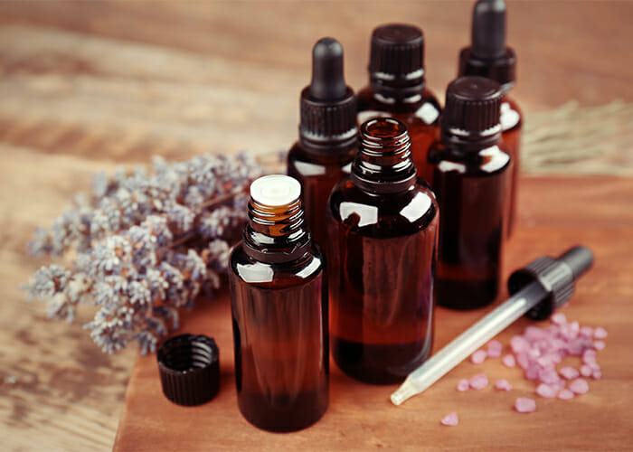 Different types of amber bottles filled with lavender essential oil on a wooden board