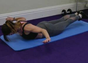 a woman face down on yoga mat with arms and legs lifted