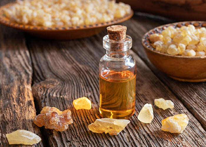 A bottle with a cork stopper filled with frankincense essential oil next to bowls of frankincense 