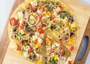 Keto breakfast pizza on a wooden board topped with cauliflowers, olives, peppers, and tomatoes