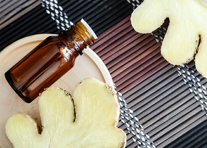 A bottle of ginger essential oil blend for digestive health next to freshly cut pieces of ginger