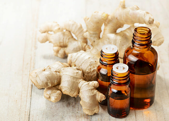 Different sized bottles of ginger essential oil blends next to fresh ginger