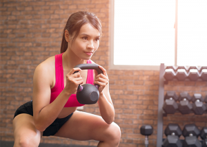 Asian woman doing a goblet squat with knees bent and holding a kettlebell
