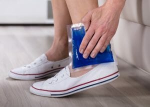 woman holding an ice pack to her ankle injury, as part of the "ice" component of the RICE injury recovery procedure