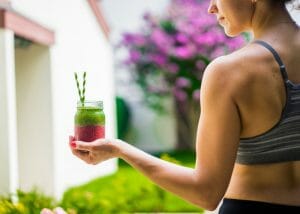 woman in sports bra holding a healthy red and green smoothie
