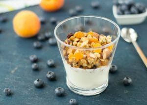 A small glass of homemade yogurt topped with mixed oats, dried fruits, and nuts