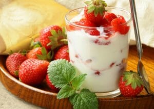 A glass of DIY yogurt with strawberries, served on a wooden tray filled with fresh strawberries