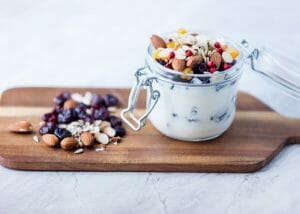 A jar of homemade yogurt on a wooden board, topped with different dried fruits and nuts