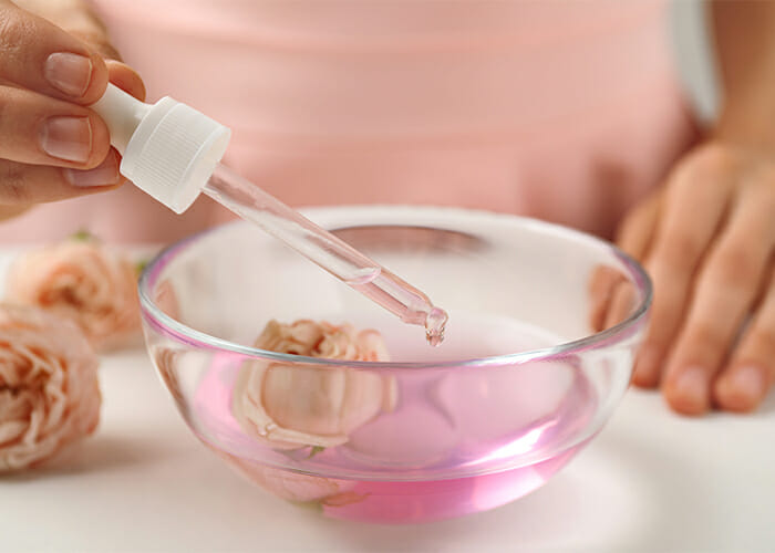 Woman using a dropper filled with carrier oil to dilute a bowl filled with rose essential oil