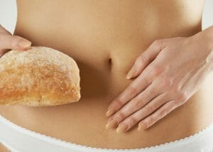 woman holding a loaf of bread with gluten in it holding her stomach to show discomfort