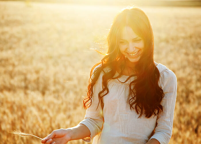 Woman smiling in a wheat field while holding a piece of wheat