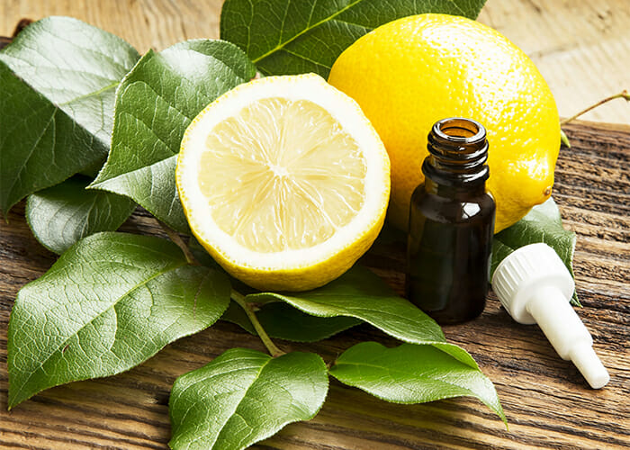 A bottle of lemon essential oil with a dropper next to whole and halved lemons