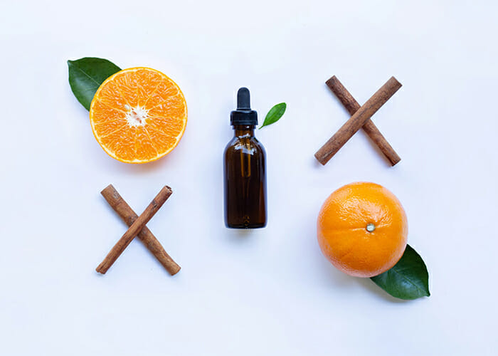 A flat lay of a vial of orange essential oil, cinnamon sticks and fresh oranges 