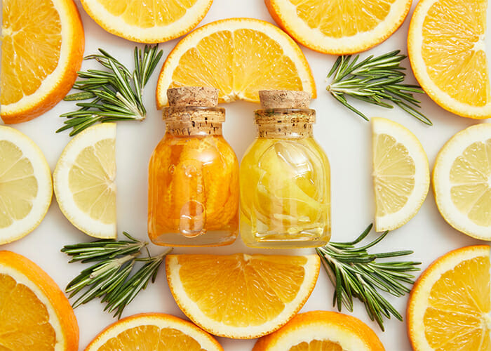 Orange and lemon essential oils blends in two small bottles surrounded by freshly cut orange and lemon pieces