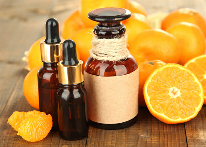Vials and a bottle of orange essential oil surrounded by fresh oranges