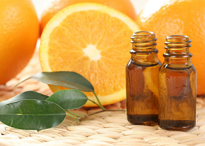 Two vials of orange essential oil in front of fresh oranges