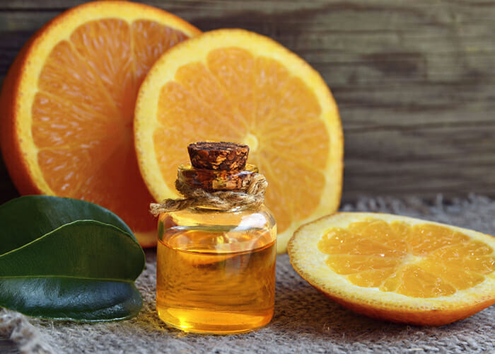 A small bottle of hand-poured orange essential oil with slices of orange in the background