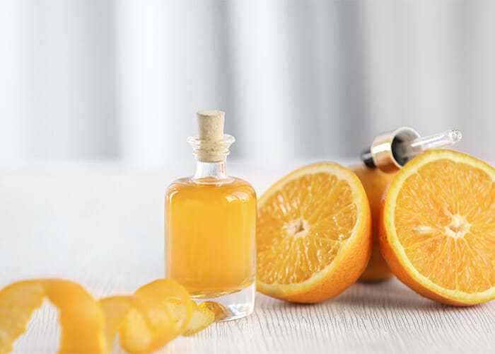 Orange essential oil in clear bottle next to a halved orange and orange rind