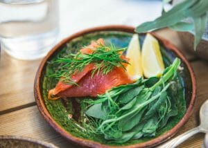 fresh greens and salmon with lemon wedges in a wooden bowl