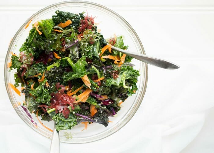 a healthy kale salad in a glass bowl on a white background