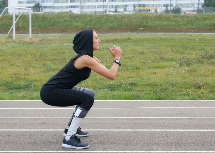 Woman in black hoodie in squatting position getting ready to do a high jump
