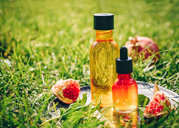 Large and small bottles of pomegranate essential oil next to pieces of pomegranate essential oil on a plate on plate on a grass