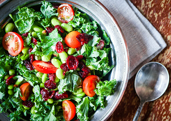 Fresh salad with leafy greens, cranberries, edamame beans, and tomatoes in a bowl 