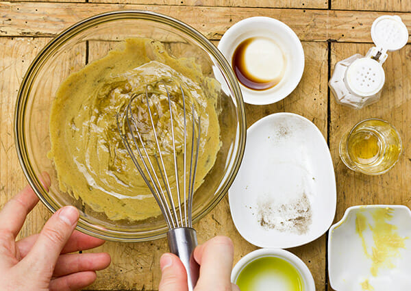 Person whisking a homemade sesame salad dressing in a bowl with small bowls of ingredients surrounding