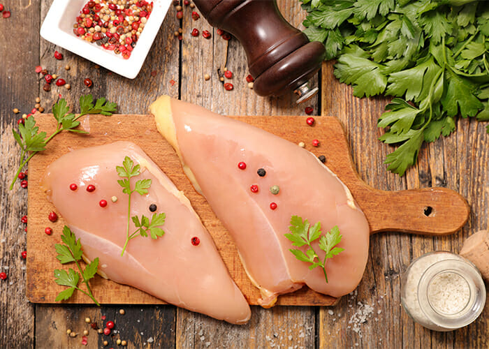 Two raw chicken breasts seasoned with pepper and herbs on a cutting board